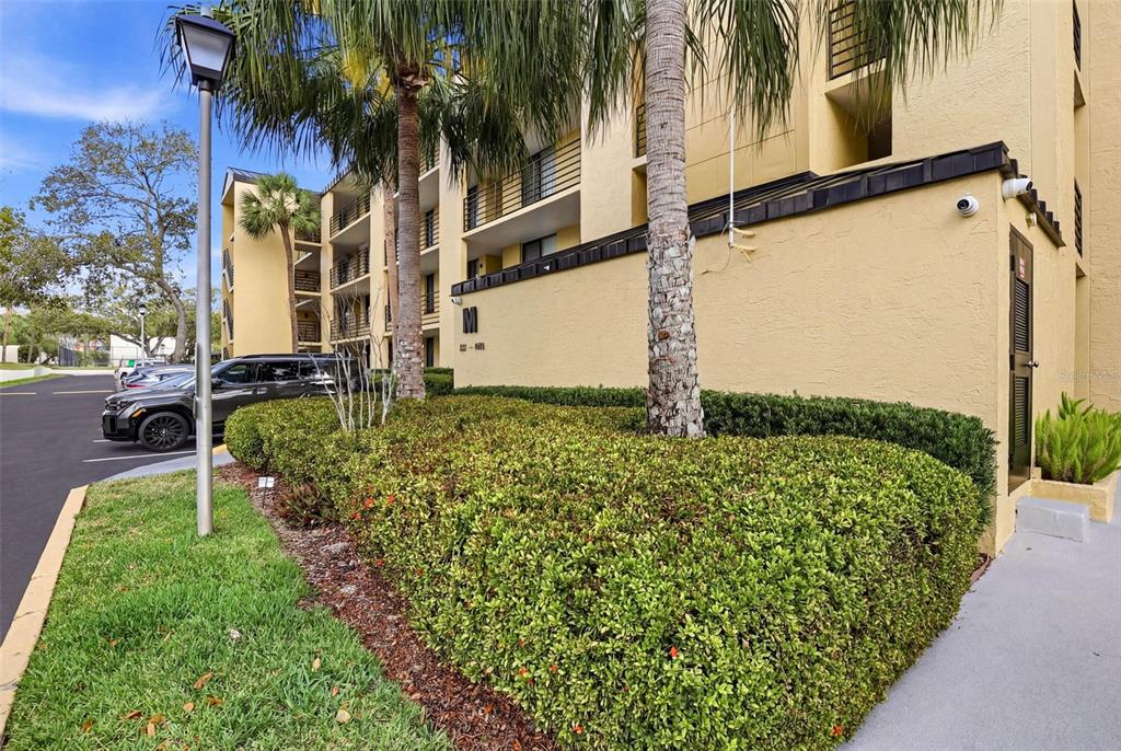 A multi-story yellow apartment building exterior features a manicured hedge and a parking area — 2424 W TAMPA BAY BOULEVARD UNIT M404, TAMPA, FL