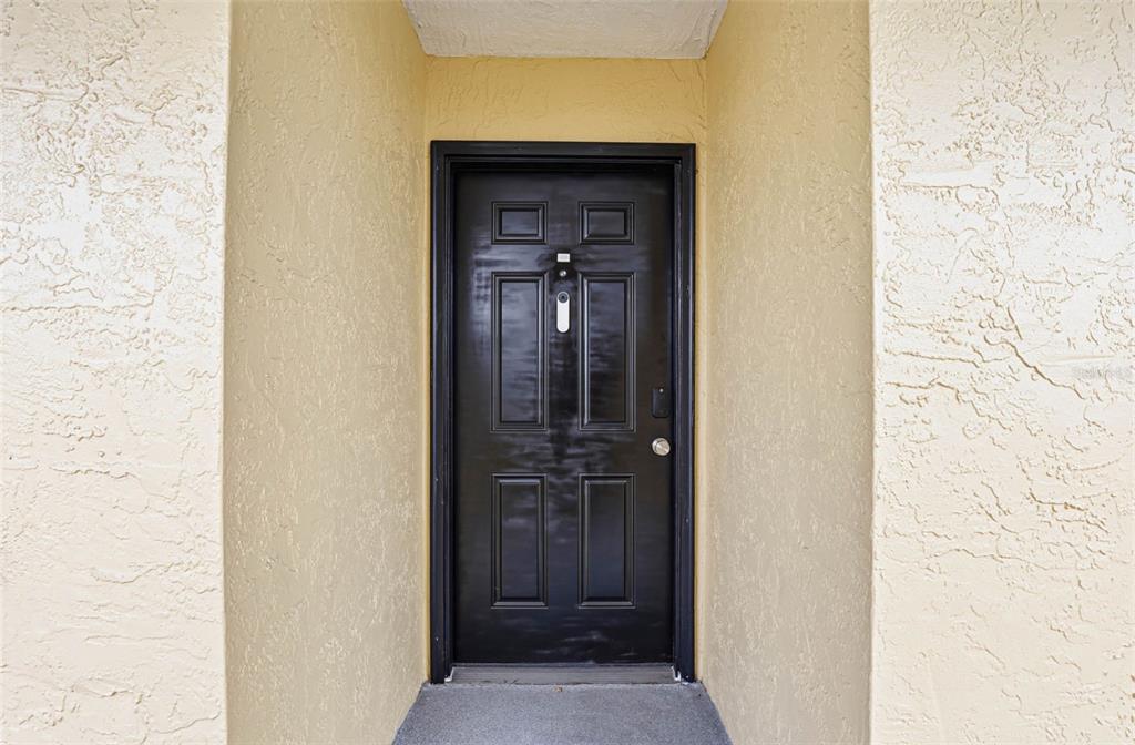 A black front door is set within a recessed entryway with textured light-colored walls — 2424 W TAMPA BAY BOULEVARD UNIT M404, TAMPA, FL