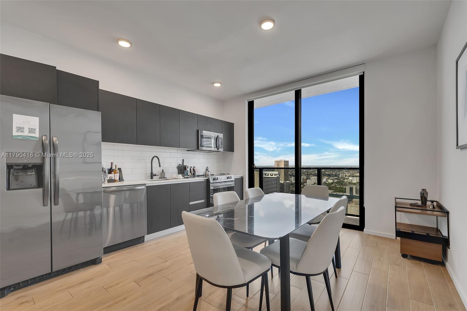 A modern kitchen and dining area features dark cabinetry, stainless steel appliances, and floor-to-ceiling windows — 398 NE 5th St # 3901, Miami FL 33132, MIAMI, FL