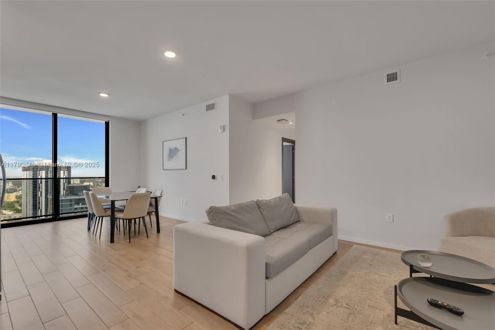 A modern living and dining area features light wood flooring, a sofa, and floor-to-ceiling windows — 398 NE 5th St # 3901, Miami FL 33132, MIAMI, FL
