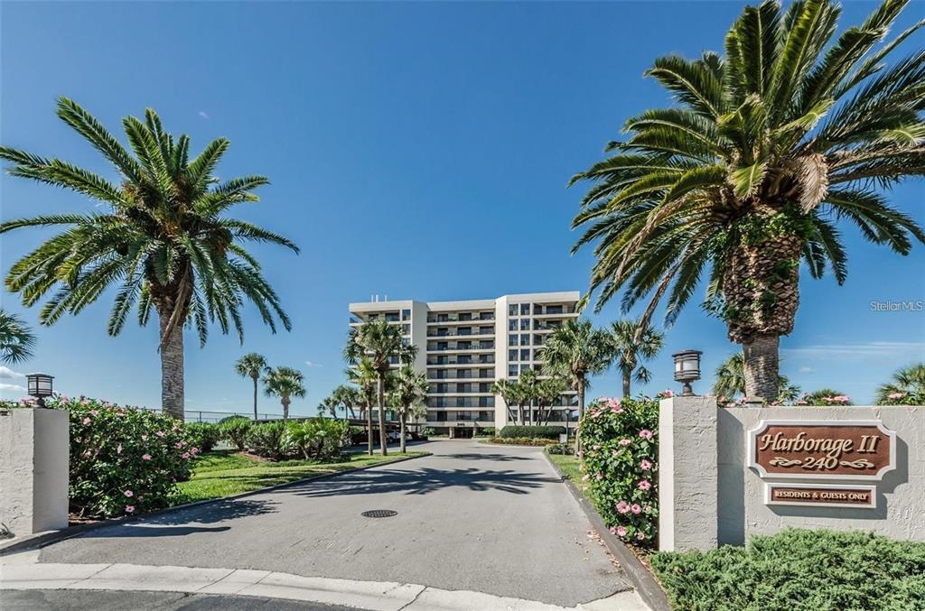 A multi-story apartment building stands behind a gated entrance with palm trees and landscaping — 240 SAND KEY ESTATES DRIVE UNIT 222, CLEARWATER, FL