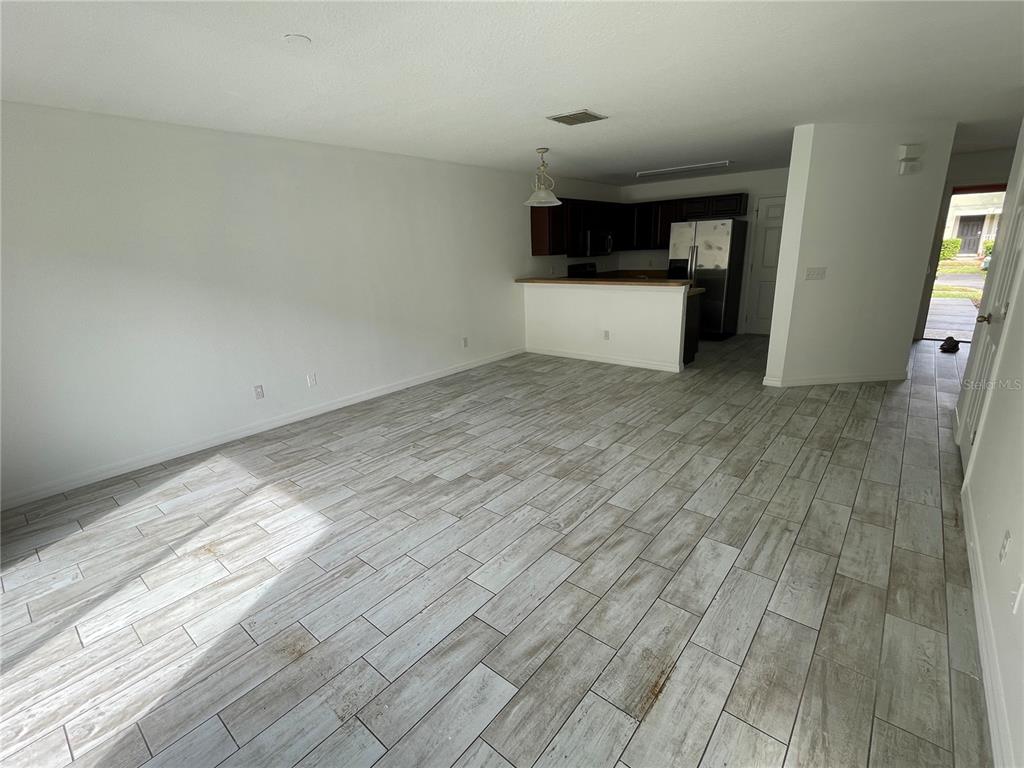 An open-concept living area features light wood-look tile flooring and a kitchen with dark cabinets — 765 CRESTING OAK CIRCLE UNIT 127, ORLANDO, FL