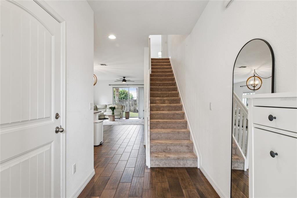 An entryway features wood-look tile flooring, a carpeted staircase, and a tall arched floor mirror — 1169 SEPIA LANE, LAKE WORTH, FL