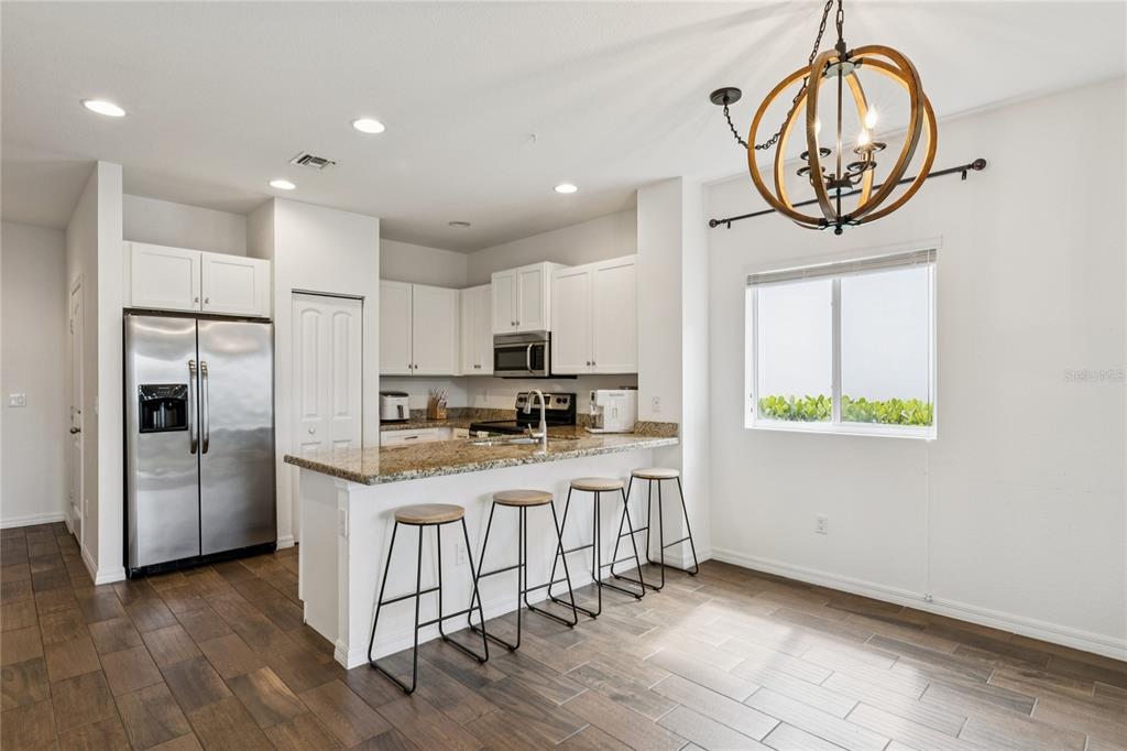 A kitchen features white cabinets, granite countertops, a stainless steel refrigerator, and four bar stools — 1169 SEPIA LANE, LAKE WORTH, FL