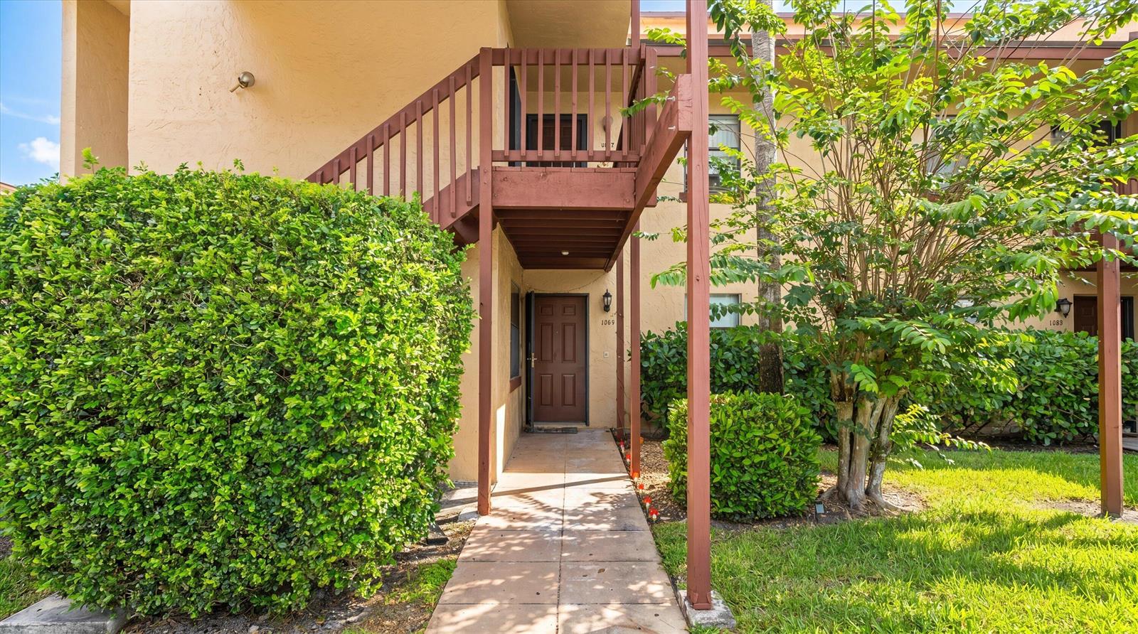 An exterior view of a ground-floor apartment entrance with a wooden staircase leading upstairs — 1303 Lakeview E, Royal Palm Beach FL 33411, ROYAL PALM BEACH, FL