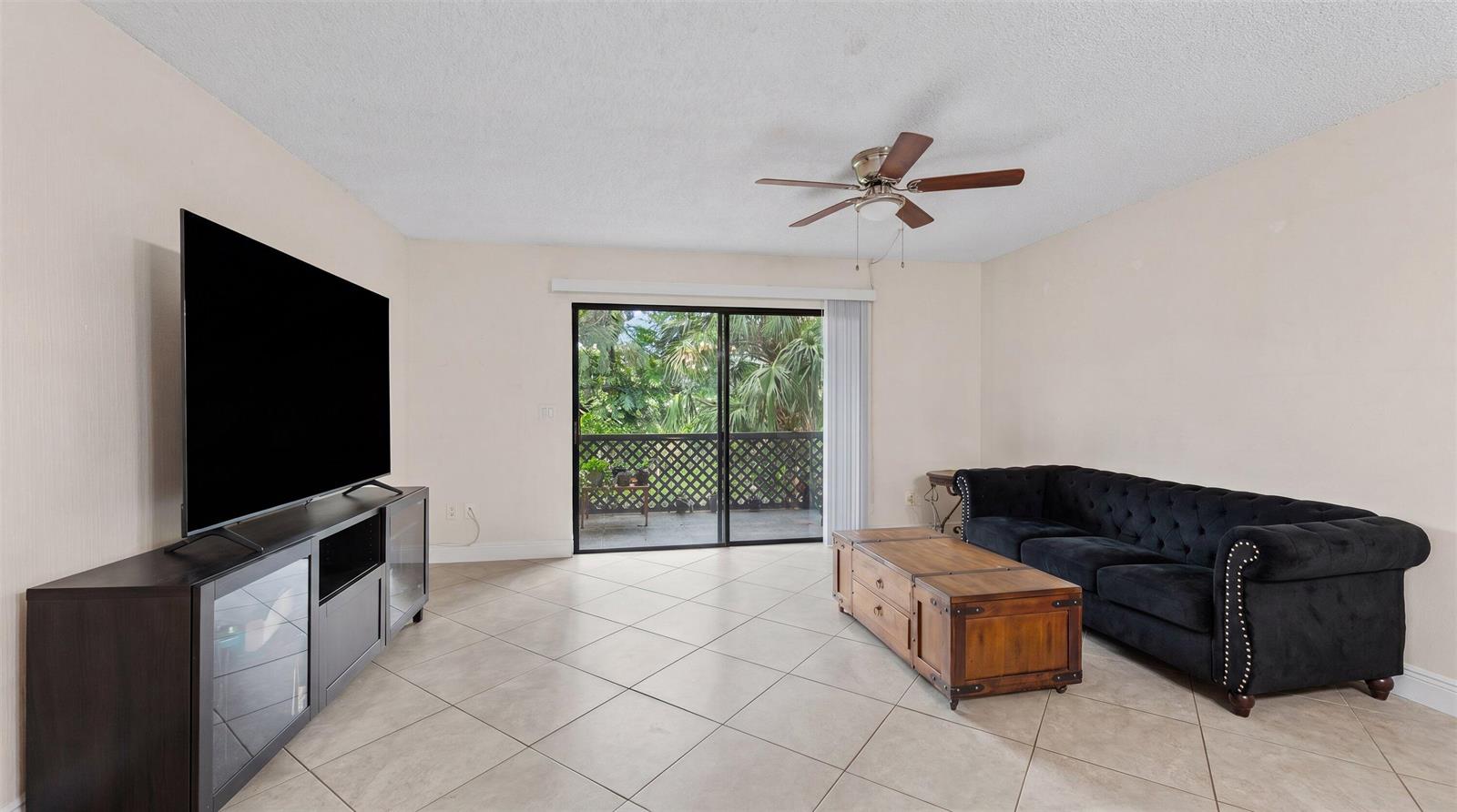 A living room features beige tile floors, a black tufted sofa, and a sliding glass door — 1303 Lakeview E, Royal Palm Beach FL 33411, ROYAL PALM BEACH, FL