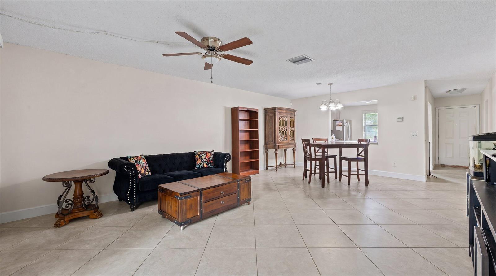 A living and dining area features tile flooring, a black tufted sofa, and wooden furniture — 1303 Lakeview E, Royal Palm Beach FL 33411, ROYAL PALM BEACH, FL