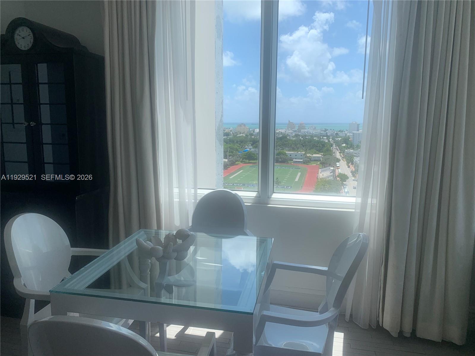 A dining area with a glass table and chairs overlooks a park and the ocean — 1100 West Ave # 1601, Miami Beach FL 33139, MIAMI BEACH, FL