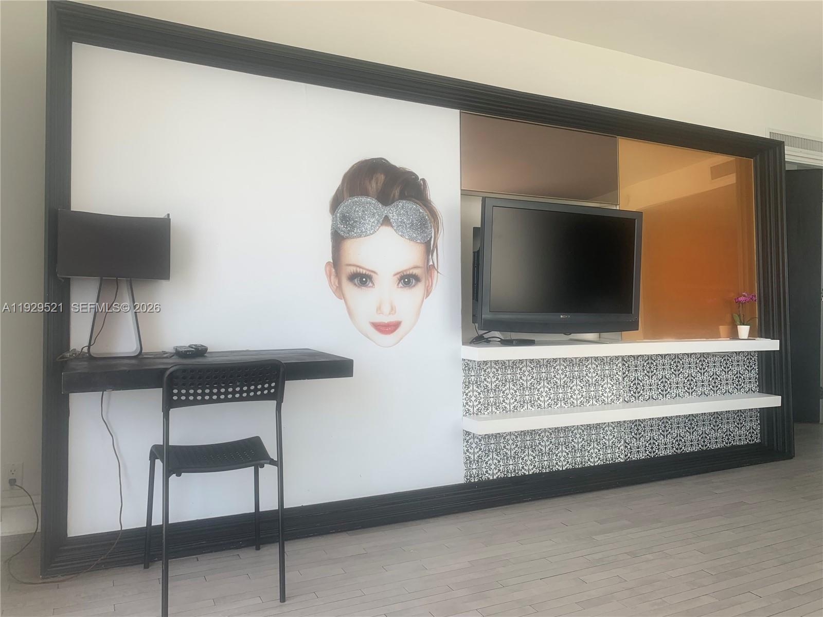 A room features a desk, a television on shelves, and a large graphic of a face — 1100 West Ave # 1601, Miami Beach FL 33139, MIAMI BEACH, FL