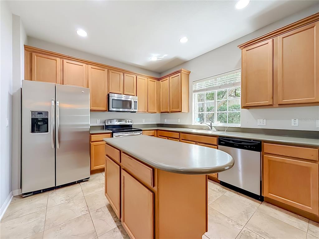 A kitchen features light wood cabinets, stainless steel appliances, a central island, and tile flooring — 2547 RIVER LANDING DRIVE, SANFORD, FL