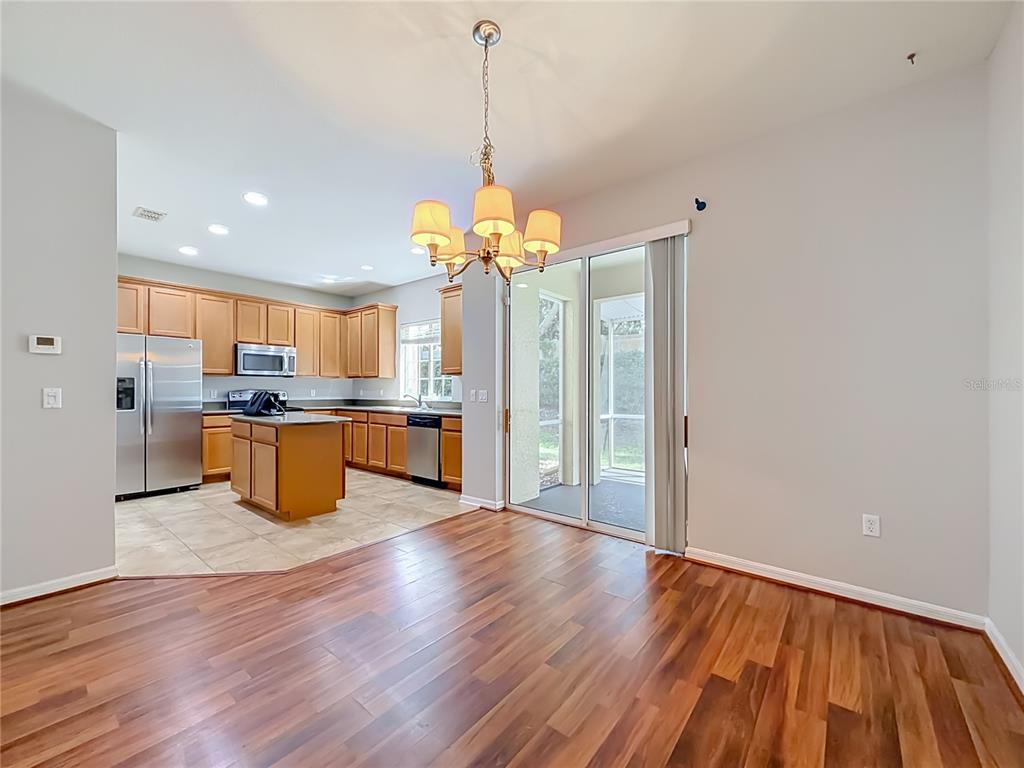 A kitchen with wood cabinets and a tile floor opens to a dining area with hardwood — 2547 RIVER LANDING DRIVE, SANFORD, FL
