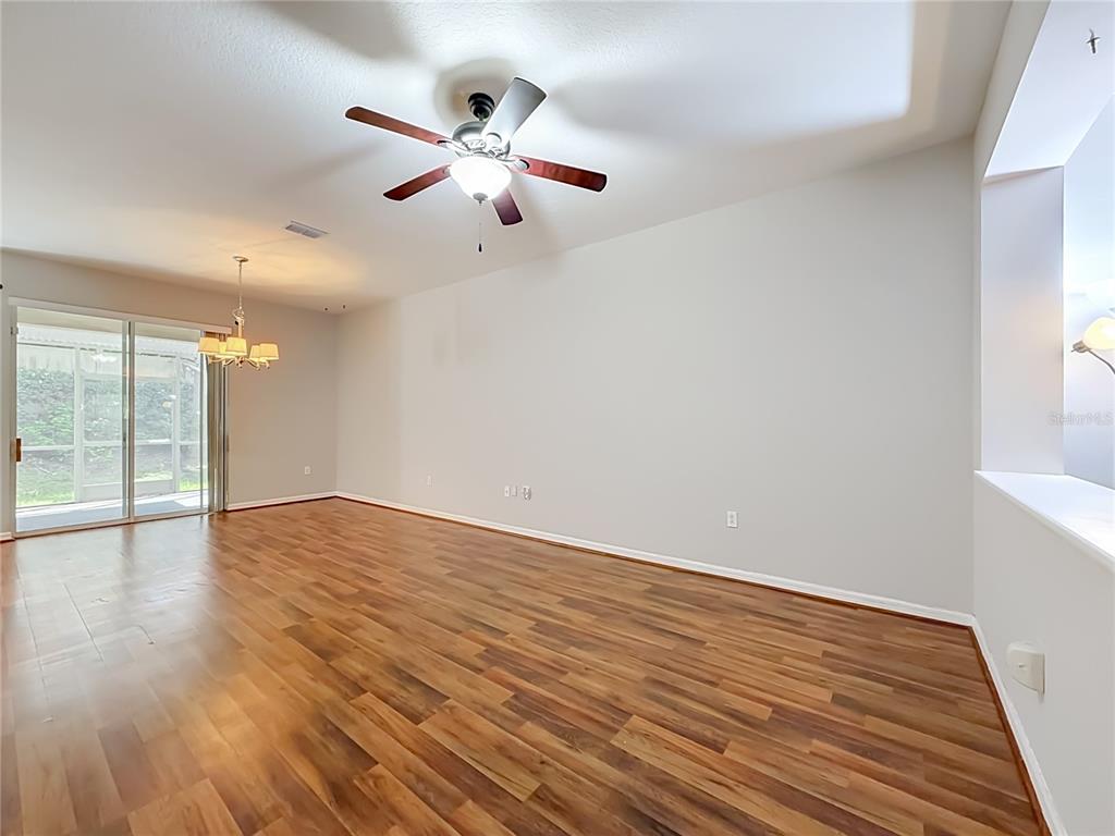An empty living room features wood-look flooring, a ceiling fan, and sliding glass patio doors — 2547 RIVER LANDING DRIVE, SANFORD, FL