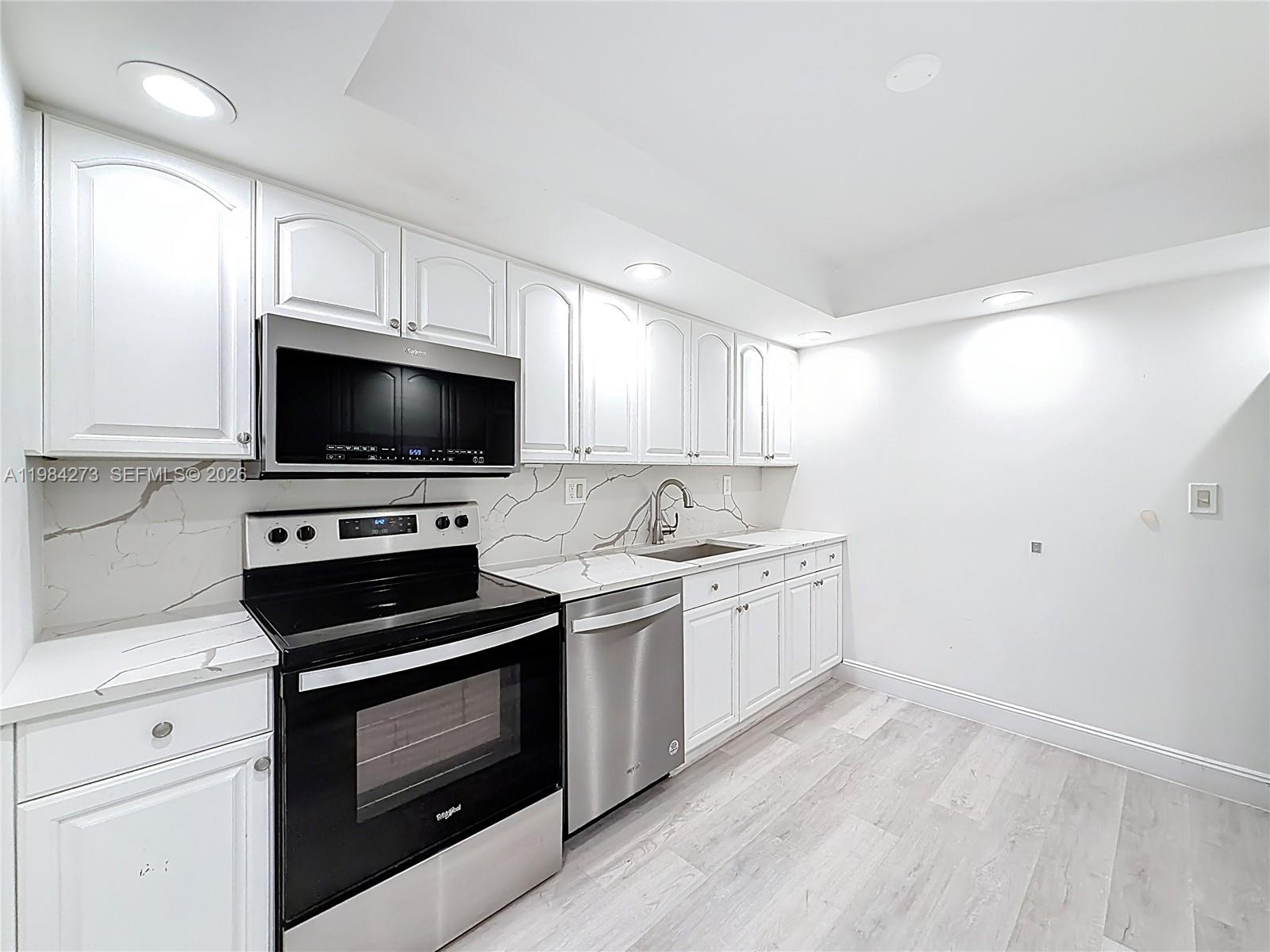 A kitchen features white cabinets, stainless steel appliances, and marble-patterned countertops and backsplash — 1000 Parkview Dr # 121, Hallandale Beach FL 33009, HALLANDALE BEACH, FL