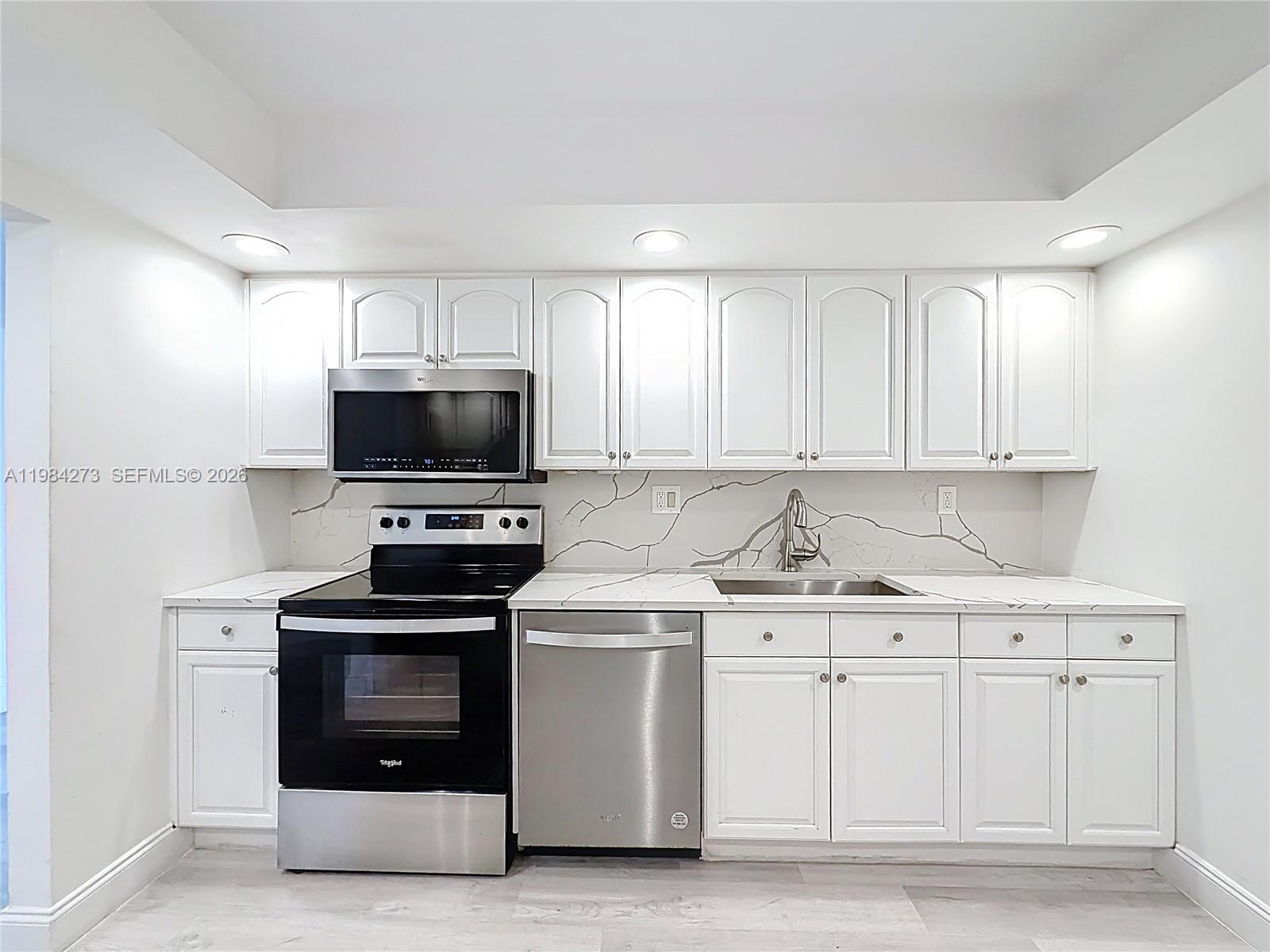 A kitchen features white cabinets, stainless steel appliances, and a marble-patterned backsplash and countertop — 1000 Parkview Dr # 121, Hallandale Beach FL 33009, HALLANDALE BEACH, FL