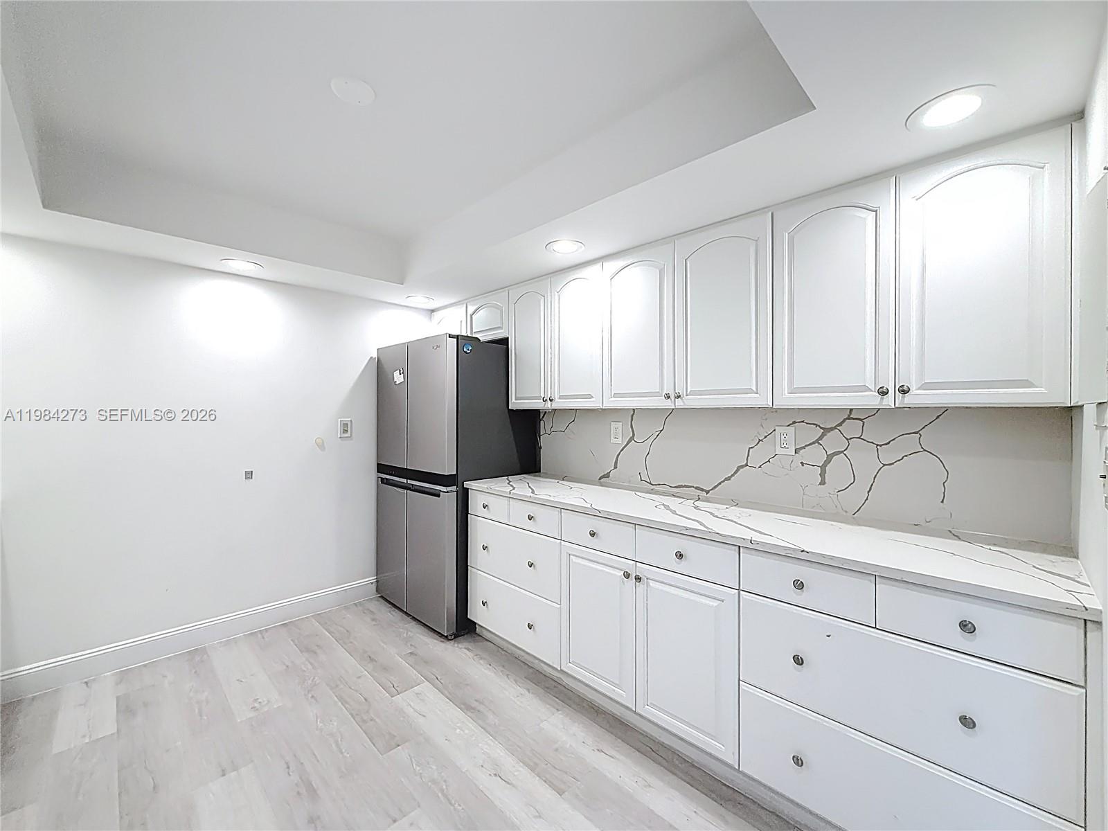 A kitchen features white cabinets, marble-patterned countertops, a backsplash, and a stainless steel refrigerator — 1000 Parkview Dr # 121, Hallandale Beach FL 33009, HALLANDALE BEACH, FL