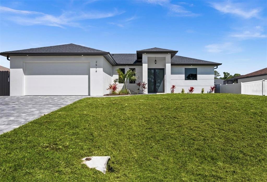 A modern, single-story white house with a two-car garage and a paved driveway — 409 NW 25TH PLACE, CAPE CORAL, FL