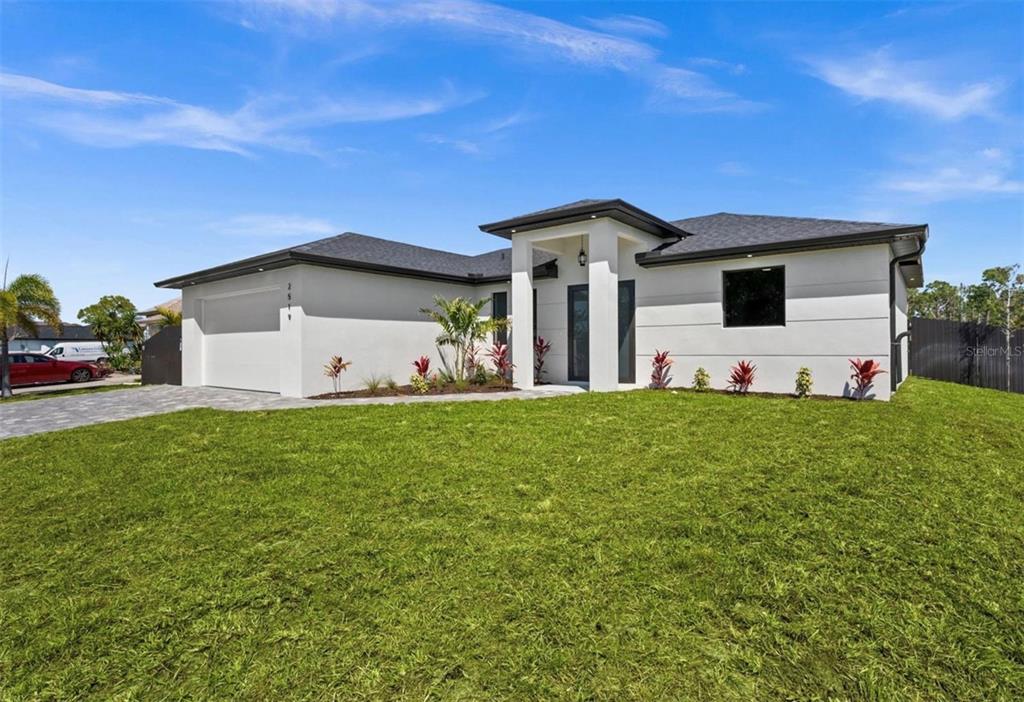 A modern, single-story white house with a dark roof and a paved driveway — 409 NW 25TH PLACE, CAPE CORAL, FL