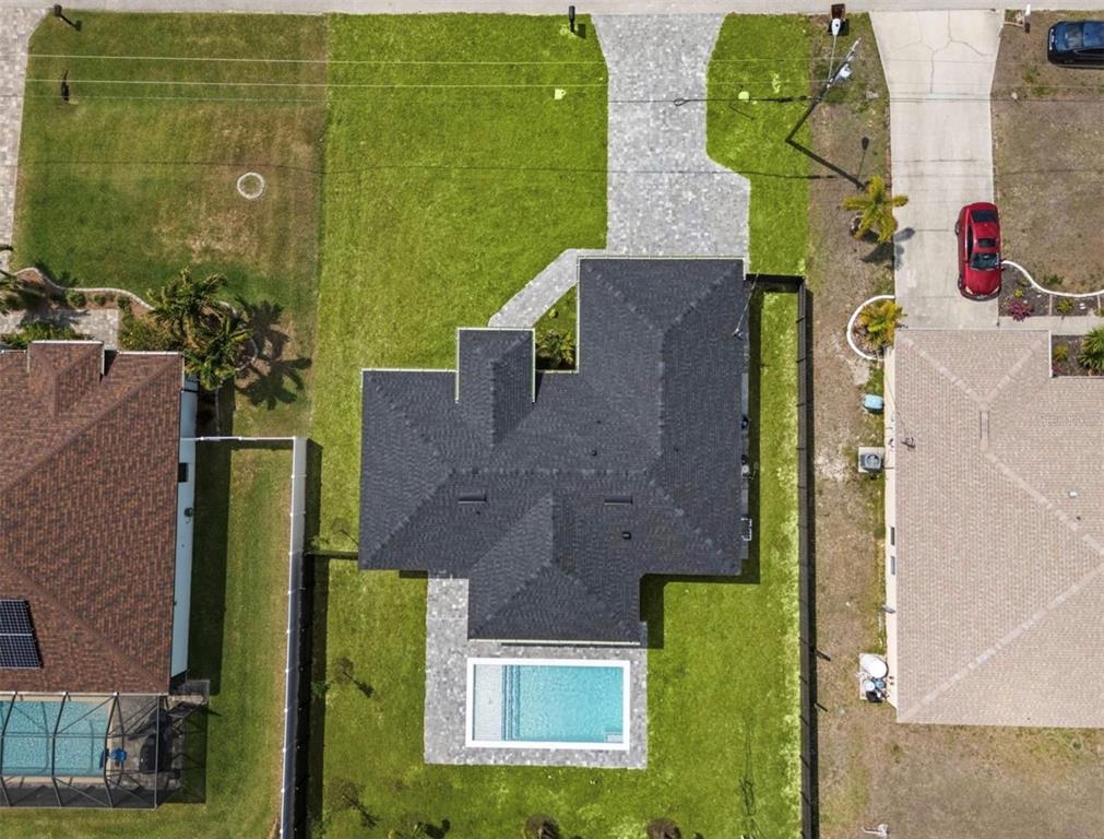 An aerial view shows a house with a dark roof, a pool, and a paved driveway — 409 NW 25TH PLACE, CAPE CORAL, FL