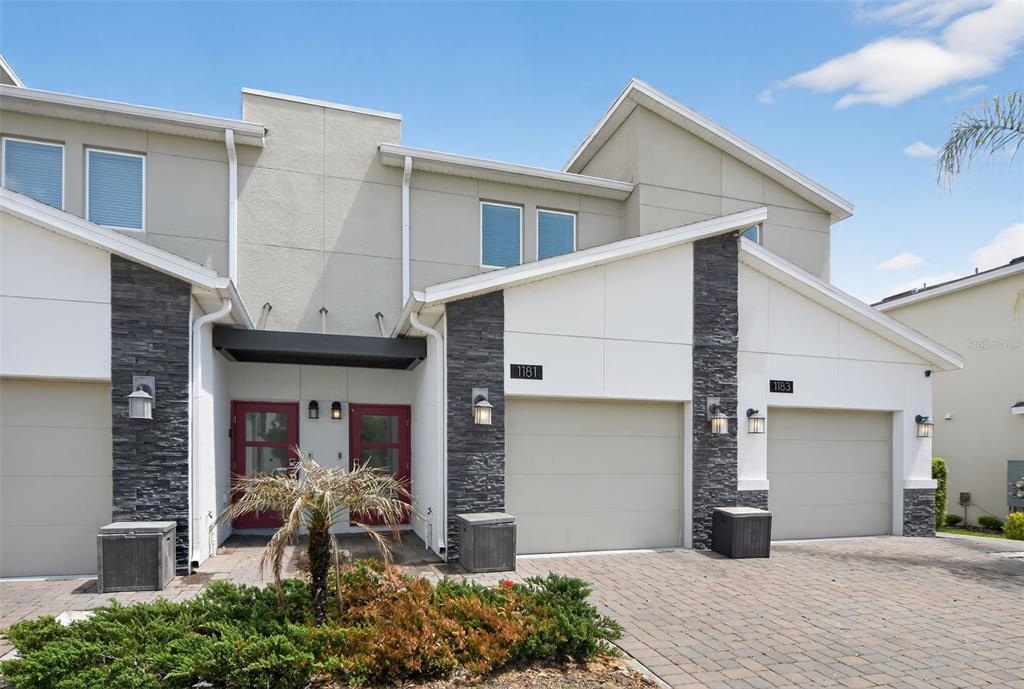The exterior of two adjacent townhomes features stone accents, beige garage doors, and red entry doors — 1181 DROP LANE UNIT 0, DAVENPORT, FL