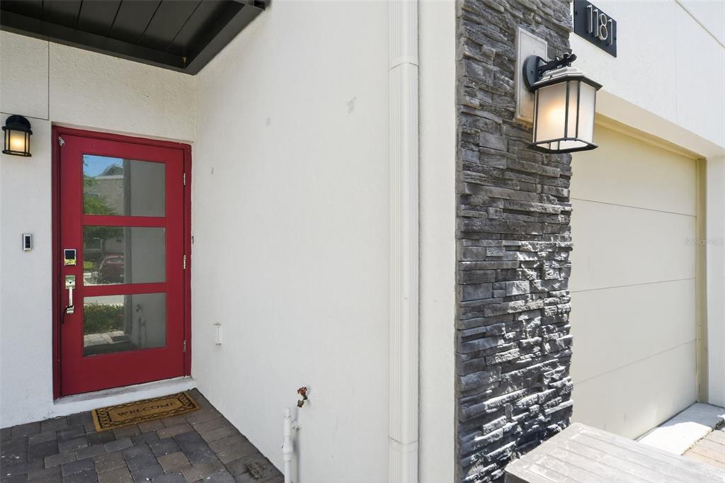 A red front door sits next to a stone-accented wall and a beige garage door — 1181 DROP LANE UNIT 0, DAVENPORT, FL