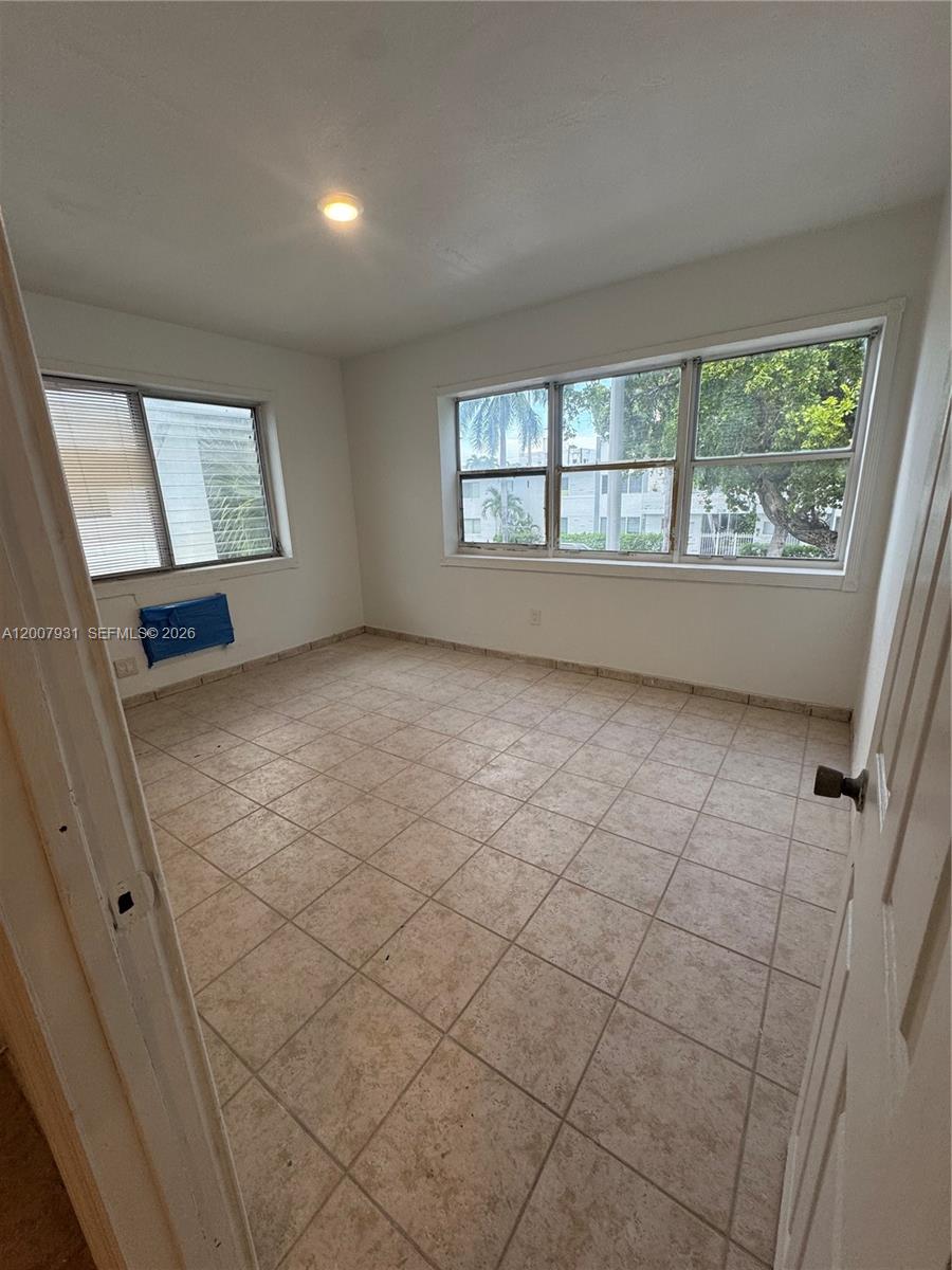An empty room features beige tile flooring, white walls, and large windows with exterior views — 7300 Harding Ave # 21, Miami Beach FL 33141, MIAMI BEACH, FL