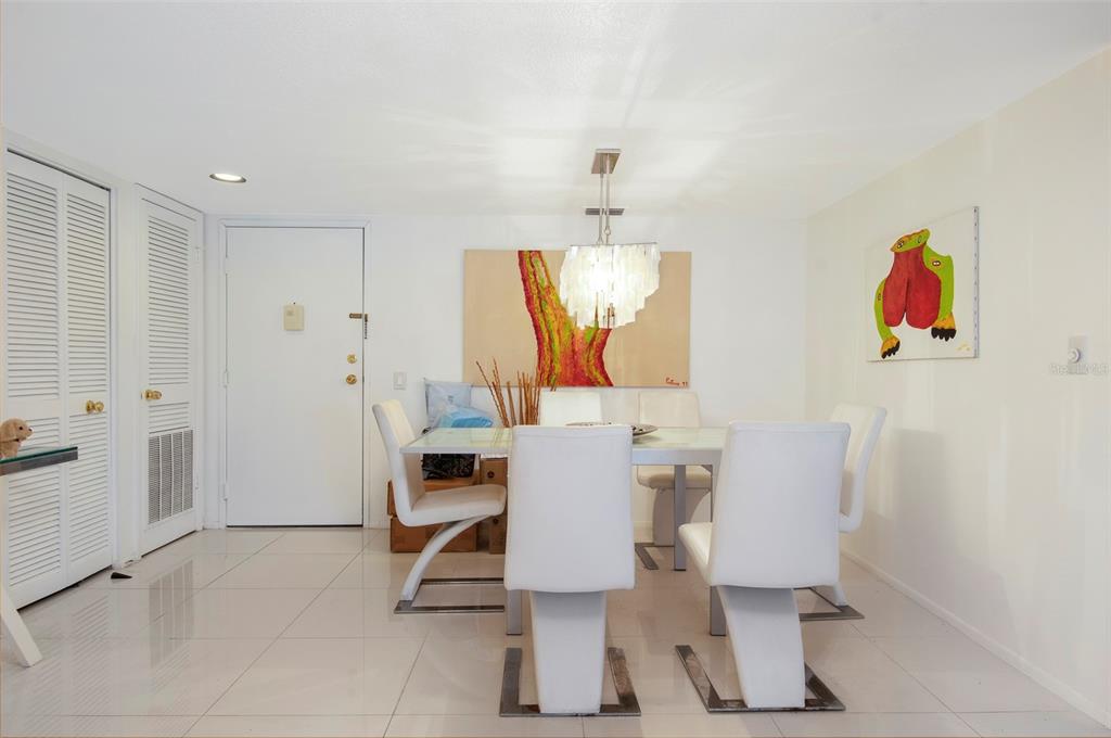 A dining room features a glass table, white chairs, a chandelier, and two wall paintings — 2593 COUNTRYSIDE BOULEVARD UNIT 7313, CLEARWATER, FL