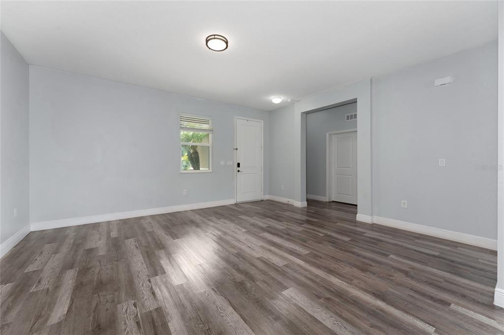 An empty room with light gray walls, wood-look flooring, a white door, and a doorway — 12845 SAWGRASS PINE CIRCLE, ORLANDO, FL