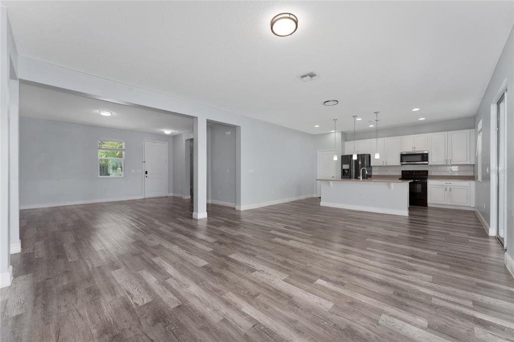 An open-concept living area features gray wood-look flooring, white walls, and a kitchen with white cabinetry — 12845 SAWGRASS PINE CIRCLE, ORLANDO, FL