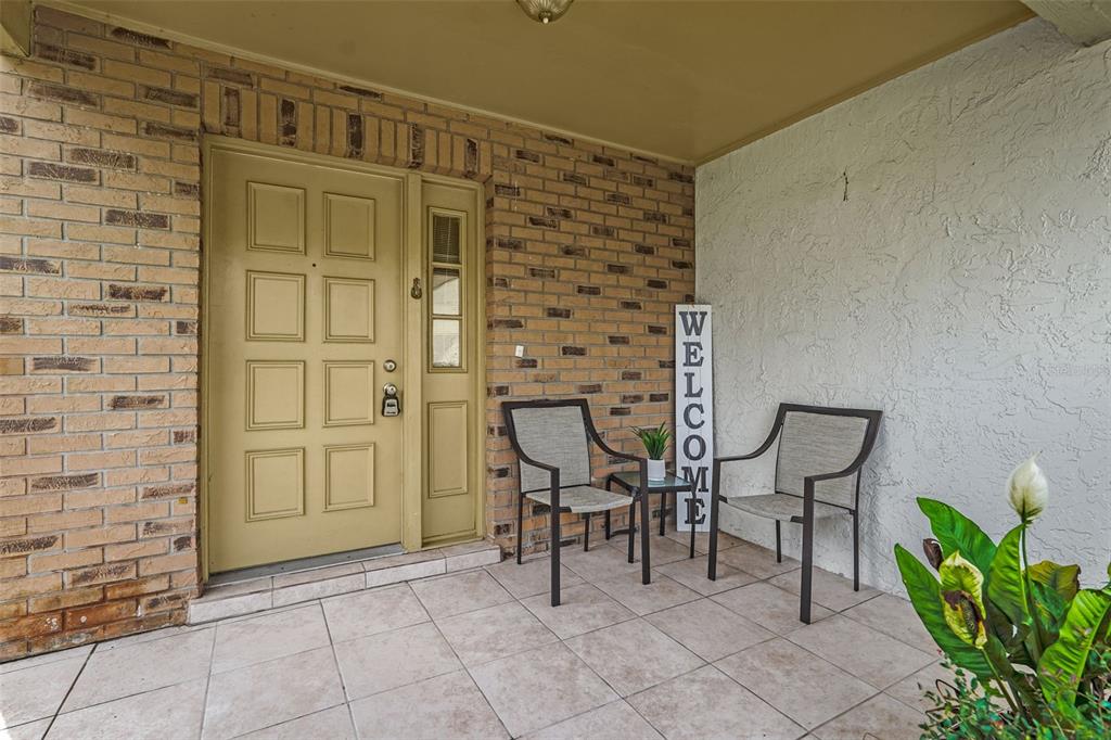A covered brick porch features a tan front door, two chairs, and a welcome sign — 2807 SUNBRANCH DRIVE, ORLANDO, FL