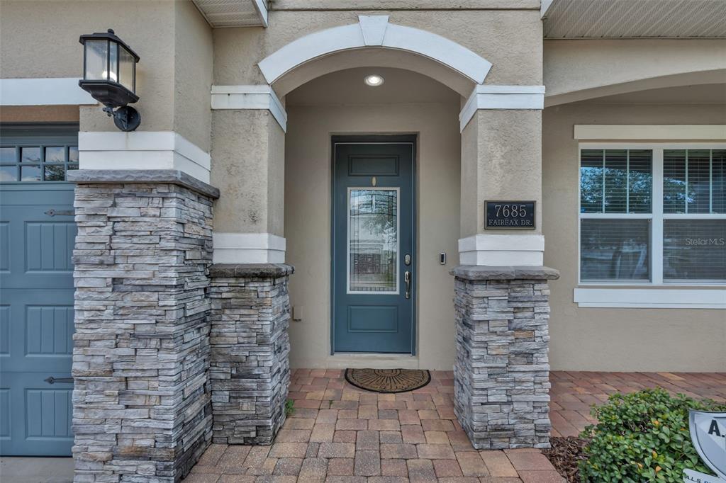 The front exterior of a house features a stone-accented entryway with a blue door — 7685 FAIRFAX DRIVE, KISSIMMEE, FL