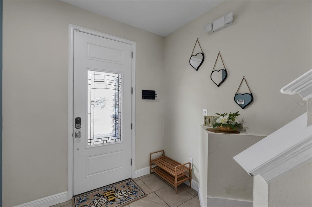 An entryway features a white front door, a wooden shoe rack, and three heart-shaped wall decorations — 7685 FAIRFAX DRIVE, KISSIMMEE, FL