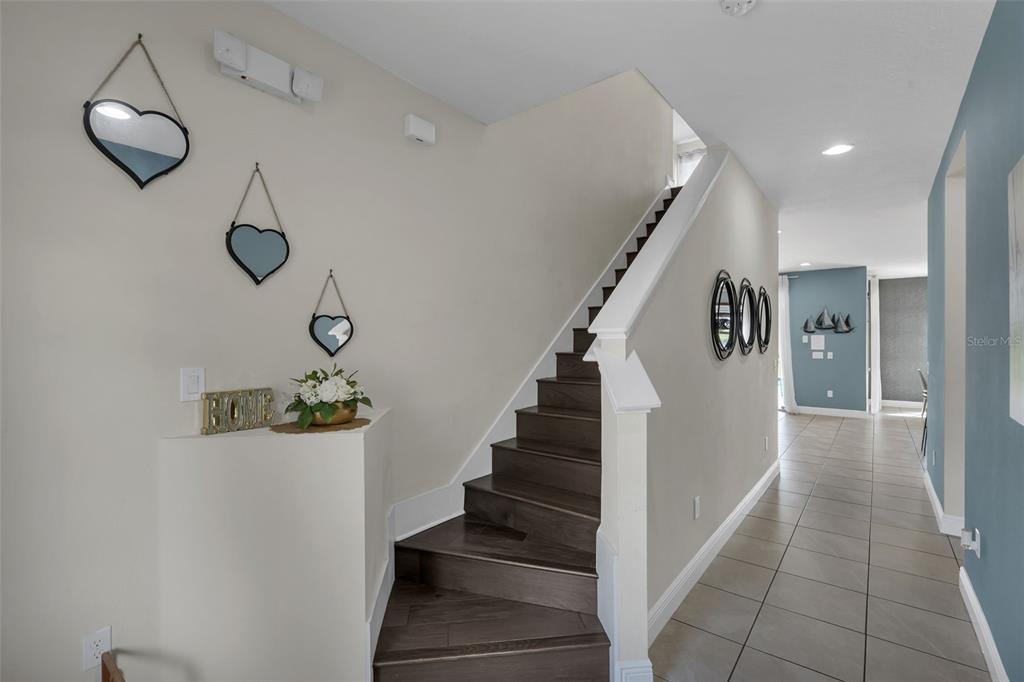 A staircase with dark wood treads leads upward next to a tiled hallway — 7685 FAIRFAX DRIVE, KISSIMMEE, FL