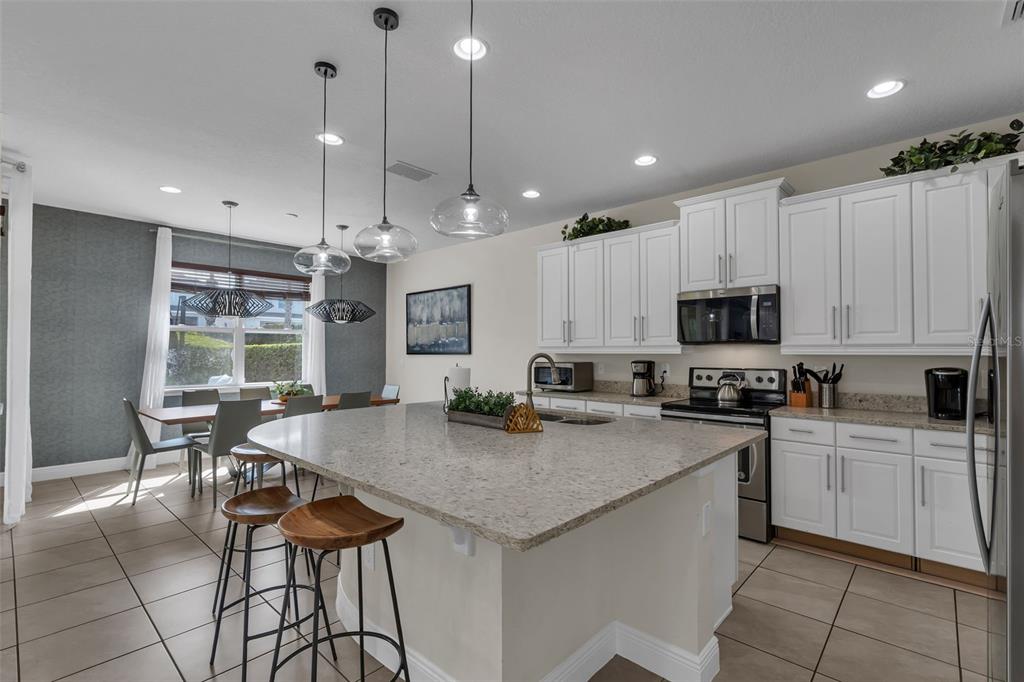 A kitchen with white cabinets, granite countertops, a large island, and an adjacent dining area — 7685 FAIRFAX DRIVE, KISSIMMEE, FL
