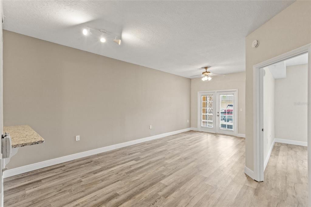 An empty living room features light wood-look flooring, beige walls, a ceiling fan, and French doors — 10855 WINDSOR WALK DRIVE UNIT 5107, ORLANDO, FL