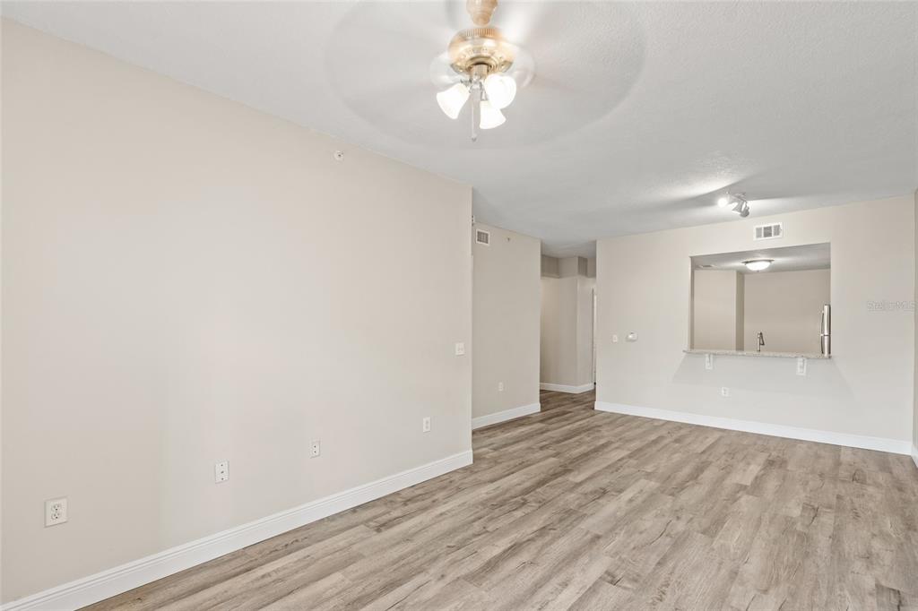 An empty room with light-colored walls, wood-look flooring, a ceiling fan, and a kitchen pass-through — 10855 WINDSOR WALK DRIVE UNIT 5107, ORLANDO, FL