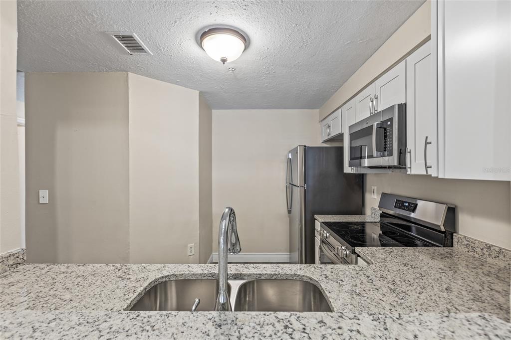 A kitchen features white cabinets, granite countertops, stainless steel appliances, and a double-basin sink — 10855 WINDSOR WALK DRIVE UNIT 5107, ORLANDO, FL