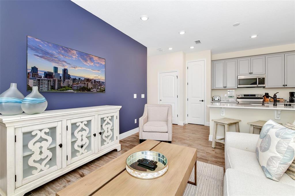 A living room with a purple accent wall, white media console, and an open kitchen — 3113 CARIBBEAN SOUL DRIVE, KISSIMMEE, FL