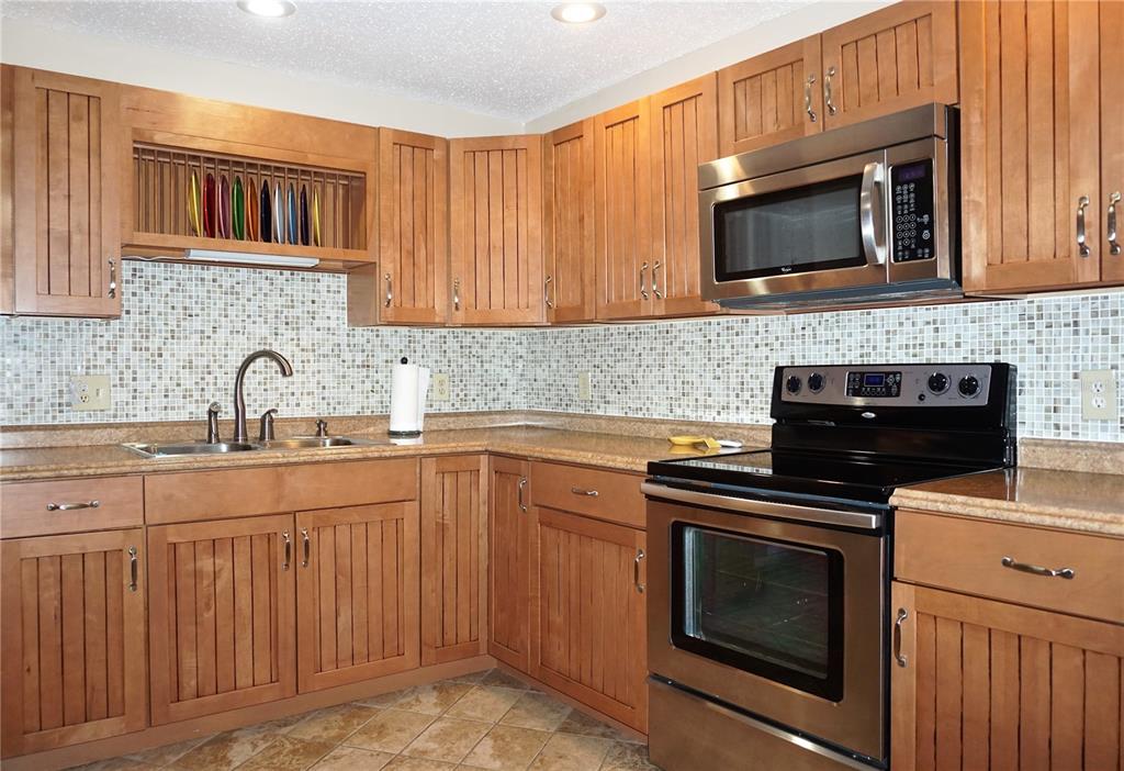 A kitchen features wood cabinets, stainless steel appliances, and a mosaic tile backsplash — 4334 TAHITIAN GARDENS CIRCLE UNIT C, HOLIDAY, FL