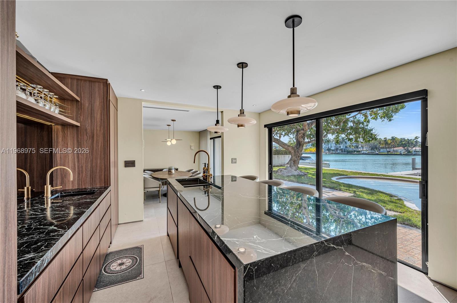 A modern kitchen features dark marble countertops, wood cabinetry, and a view of the water — 1170 S Biscayne Point Rd, Miami Beach FL 33141, MIAMI BEACH, FL