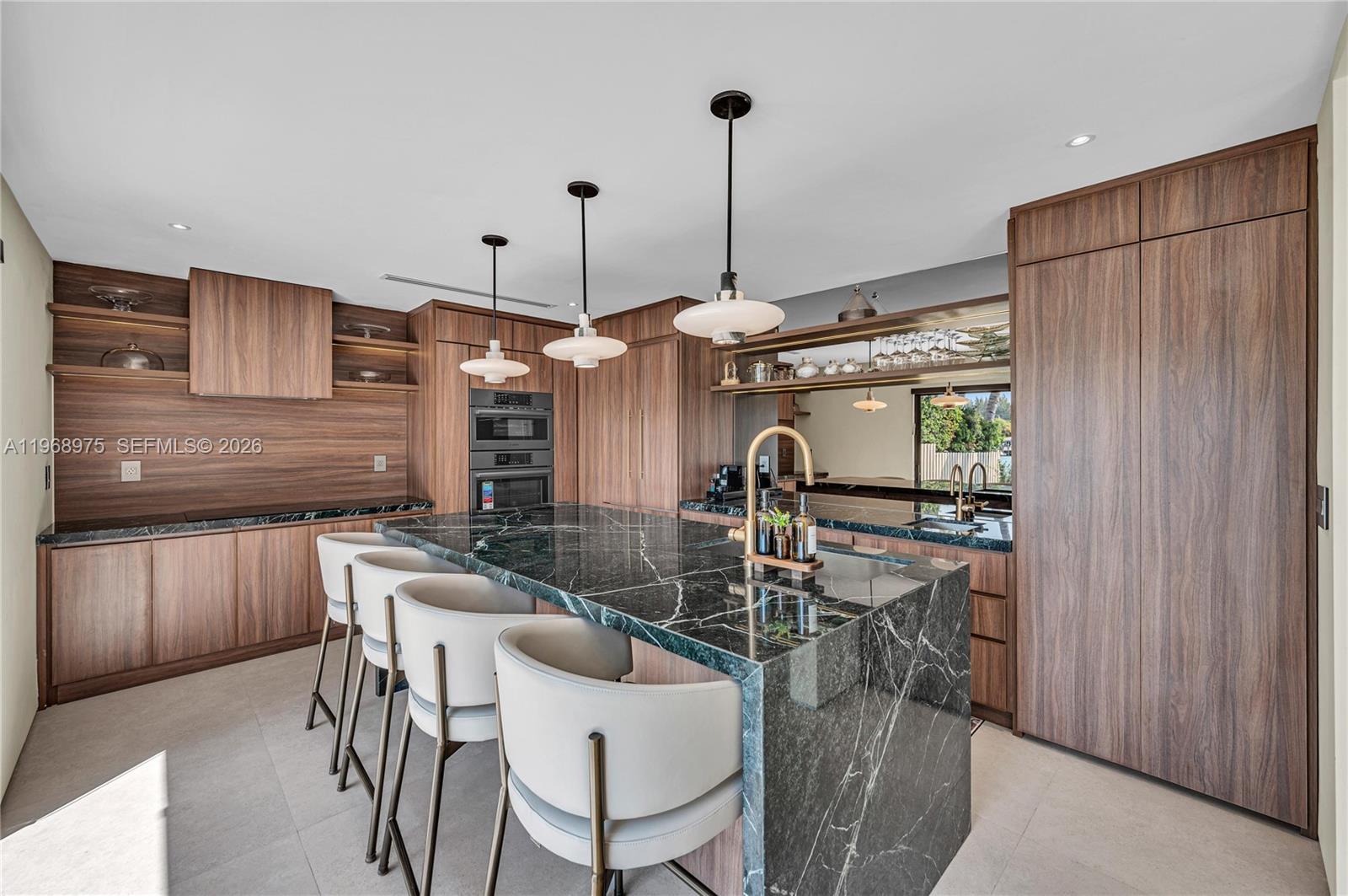 A modern kitchen features dark wood cabinetry, a large marble island, and three pendant lights — 1170 S Biscayne Point Rd, Miami Beach FL 33141, MIAMI BEACH, FL