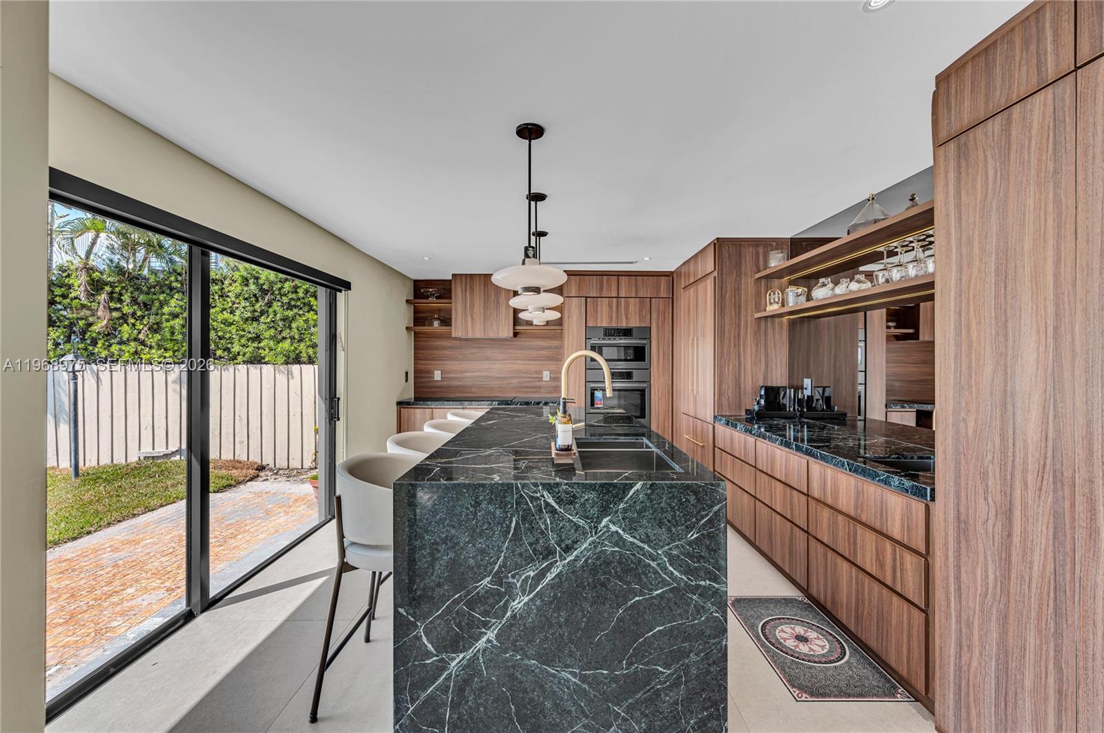 A modern kitchen features a dark green marble island, wood cabinetry, and a sliding glass door — 1170 S Biscayne Point Rd, Miami Beach FL 33141, MIAMI BEACH, FL