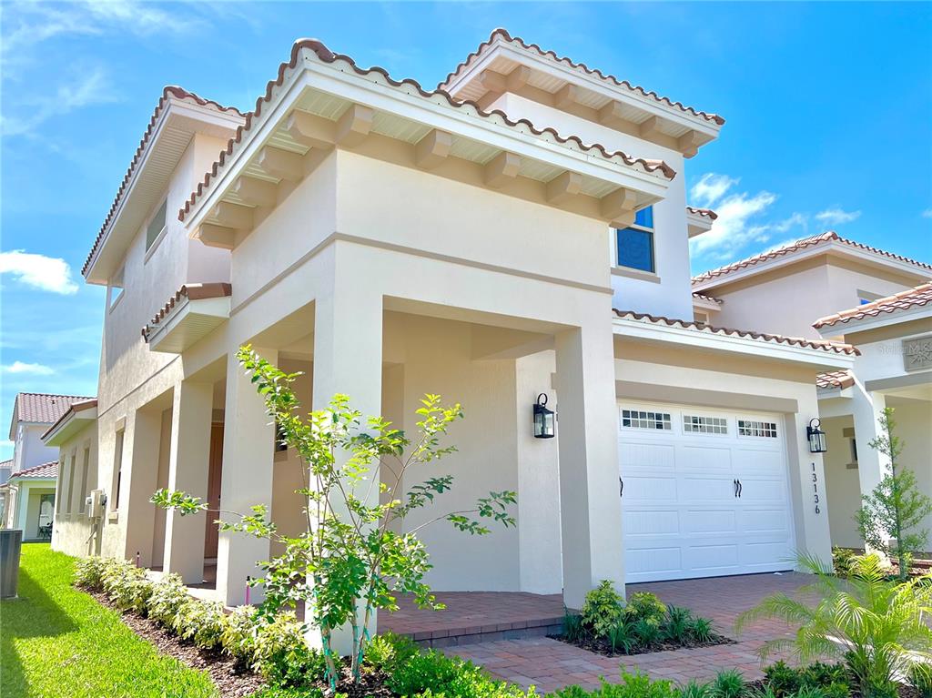 A two-story house exterior features a covered entryway, a white garage door, and tiled roofing — 13136 WEAVER AVENUE, ORLANDO, FL