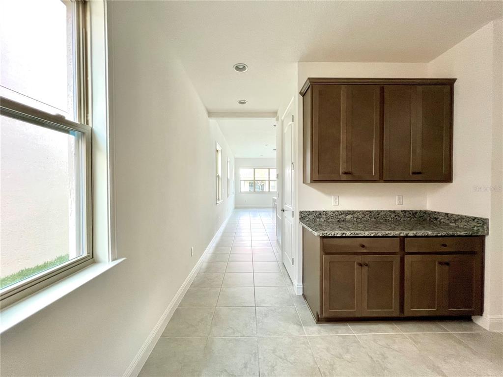 A hallway with tile flooring leads to a kitchen area featuring dark wood cabinets — 13136 WEAVER AVENUE, ORLANDO, FL