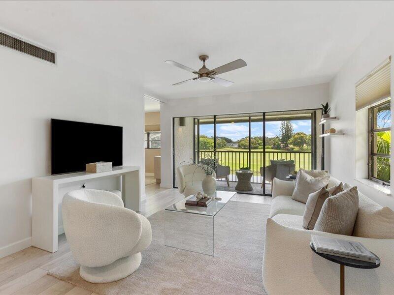 A bright living room features white furniture, a glass coffee table, and sliding doors to a balcony — 551 Greensward Lane # d, Delray Beach FL 33445, DELRAY BEACH, FL