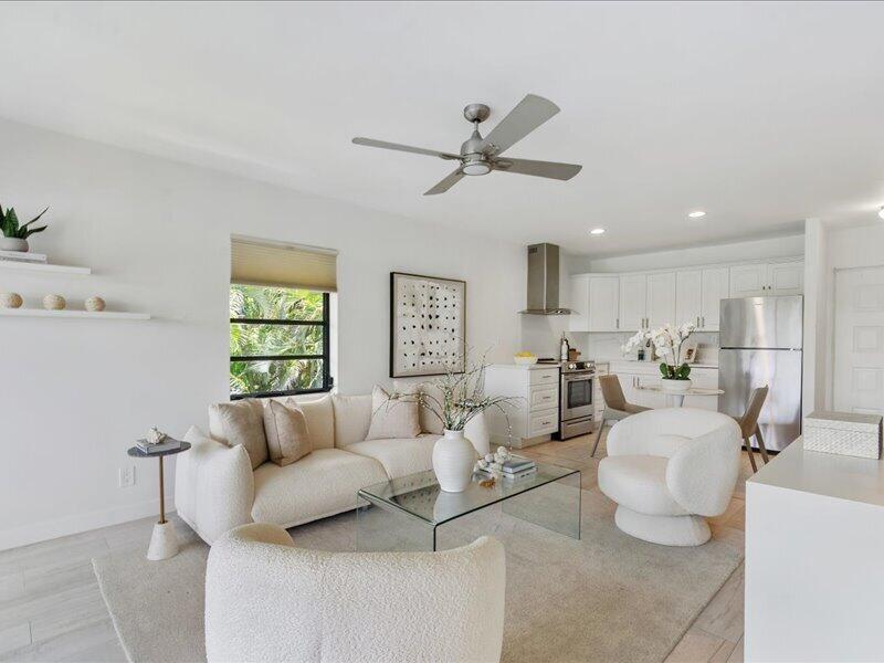 A bright open-concept living room and kitchen featuring white furniture, a glass coffee table, and stainless-steel appliances — 551 Greensward Lane # d, Delray Beach FL 33445, DELRAY BEACH, FL