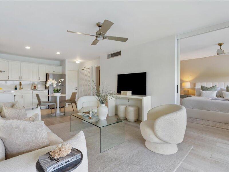 A bright, open-concept living area features white furniture, a glass coffee table, and a kitchen — 551 Greensward Lane # d, Delray Beach FL 33445, DELRAY BEACH, FL