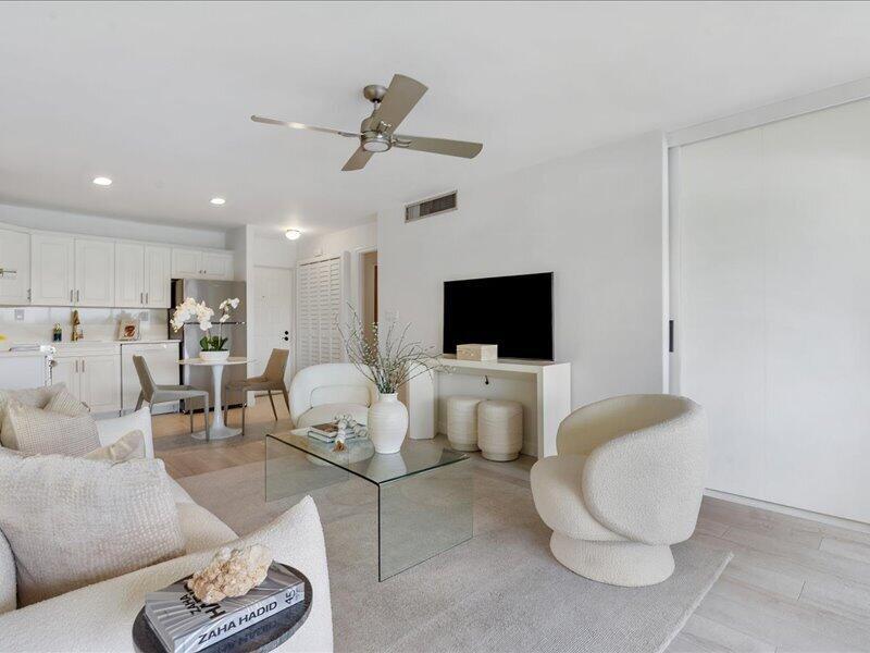 A bright living room features white furniture, a glass coffee table, and an open kitchen — 551 Greensward Lane # d, Delray Beach FL 33445, DELRAY BEACH, FL