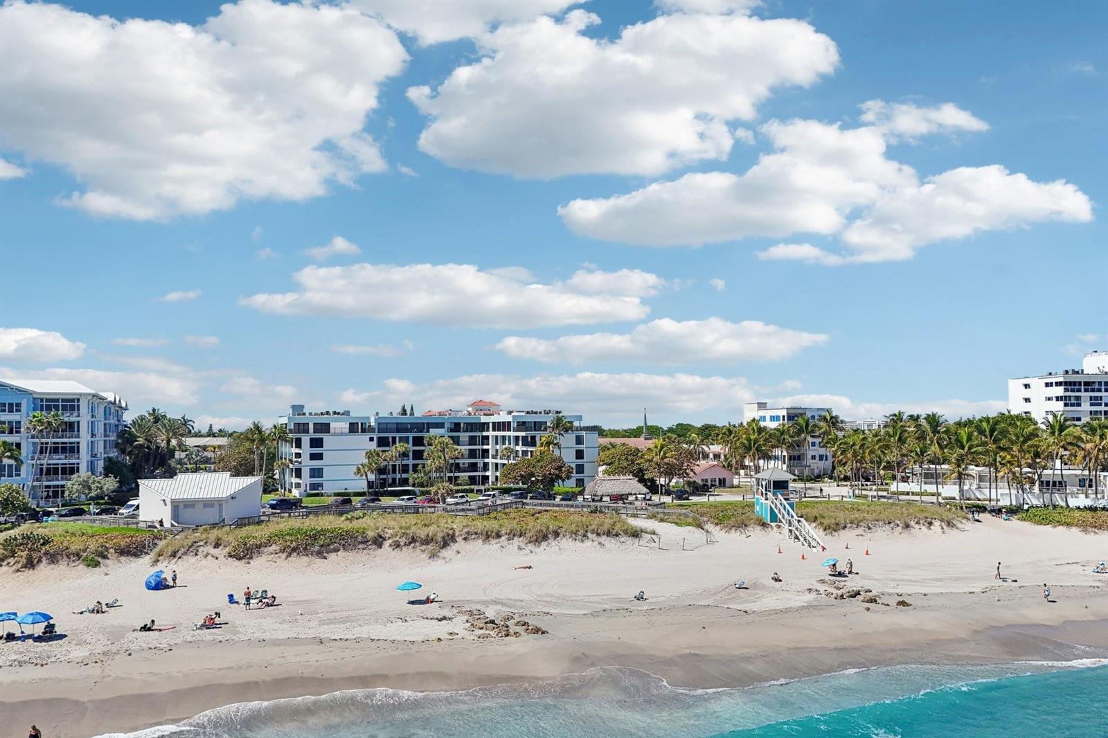An aerial view of a sandy beach with people, umbrellas, and nearby apartment buildings — 665 SE 21st Avenue # 107, Deerfield Beach FL 33441, DEERFIELD BEACH, FL