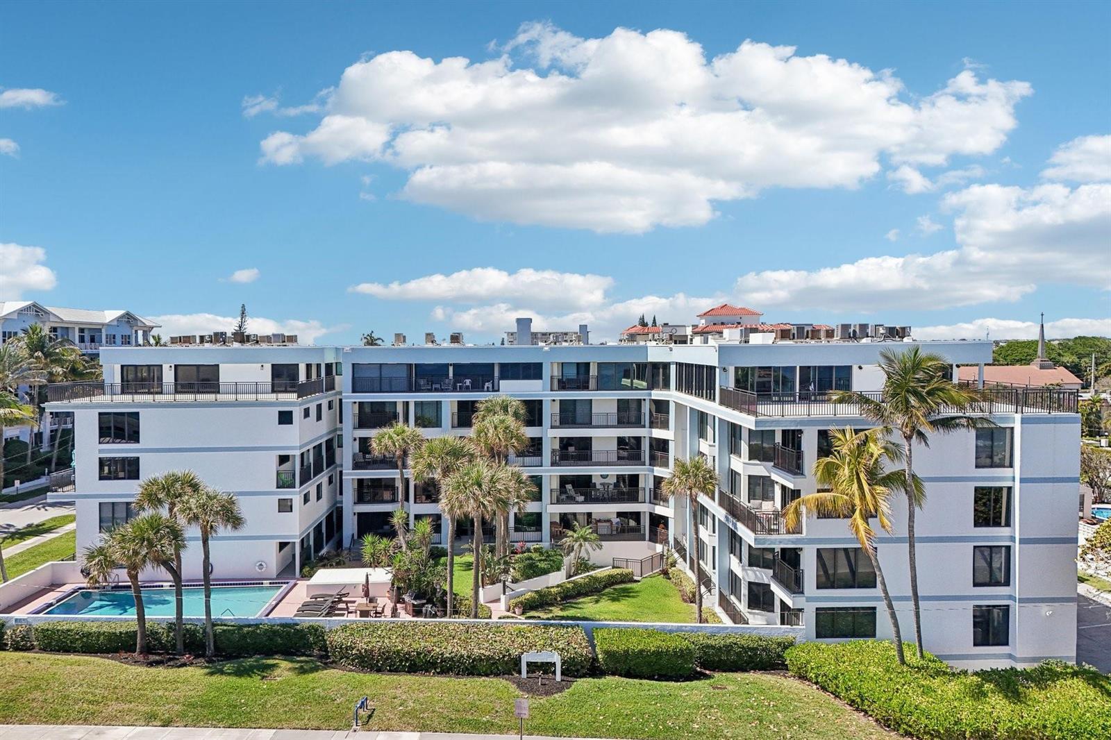 An exterior view of a multi-story apartment building with a swimming pool and palm trees — 665 SE 21st Avenue # 107, Deerfield Beach FL 33441, DEERFIELD BEACH, FL