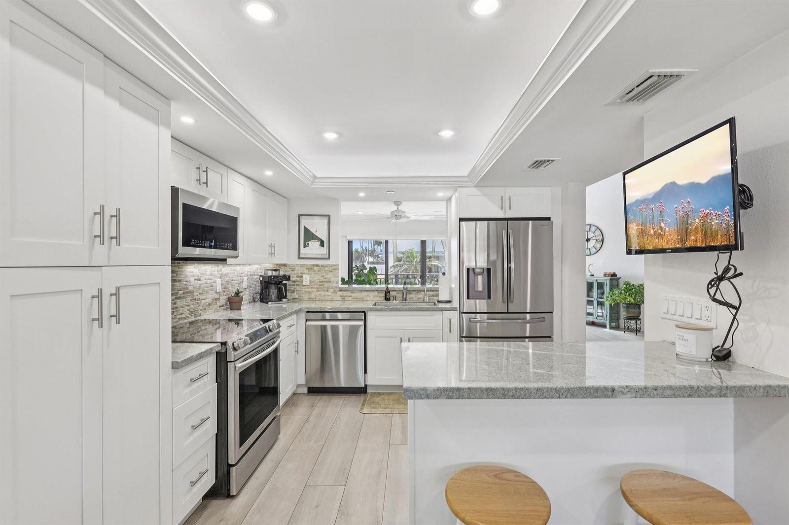 A modern kitchen features white cabinetry, stainless steel appliances, granite countertops, and a breakfast bar — 665 SE 21st Avenue # 107, Deerfield Beach FL 33441, DEERFIELD BEACH, FL